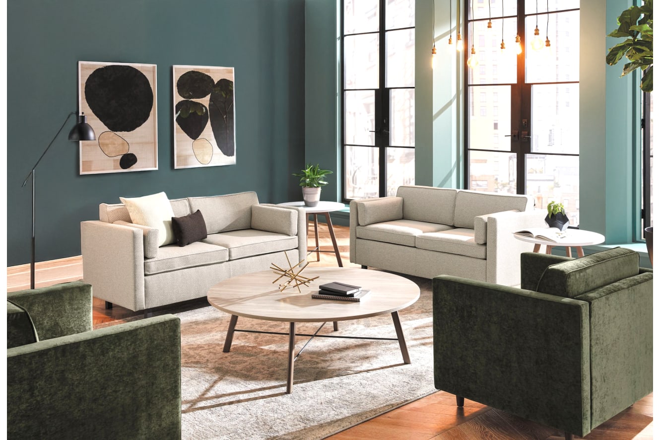 A cozy and stylish living room with neutral-toned sofas, abstract artwork on the walls, and a round wooden coffee table in the foreground, set against a backdrop of large windows and a lush indoor plant.