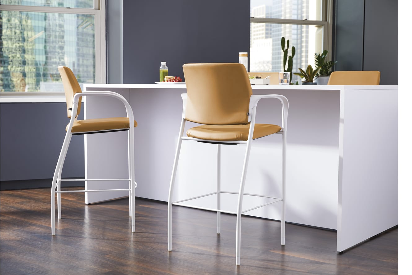 A modern kitchen with a white countertop, yellow bar stools, and a large window overlooking a cityscape.
