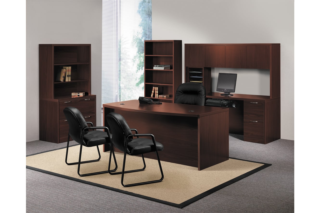A modern and minimalist home office setup with a large wooden desk, bookshelves, and black office chairs arranged in a spacious room with a large window providing natural lighting.