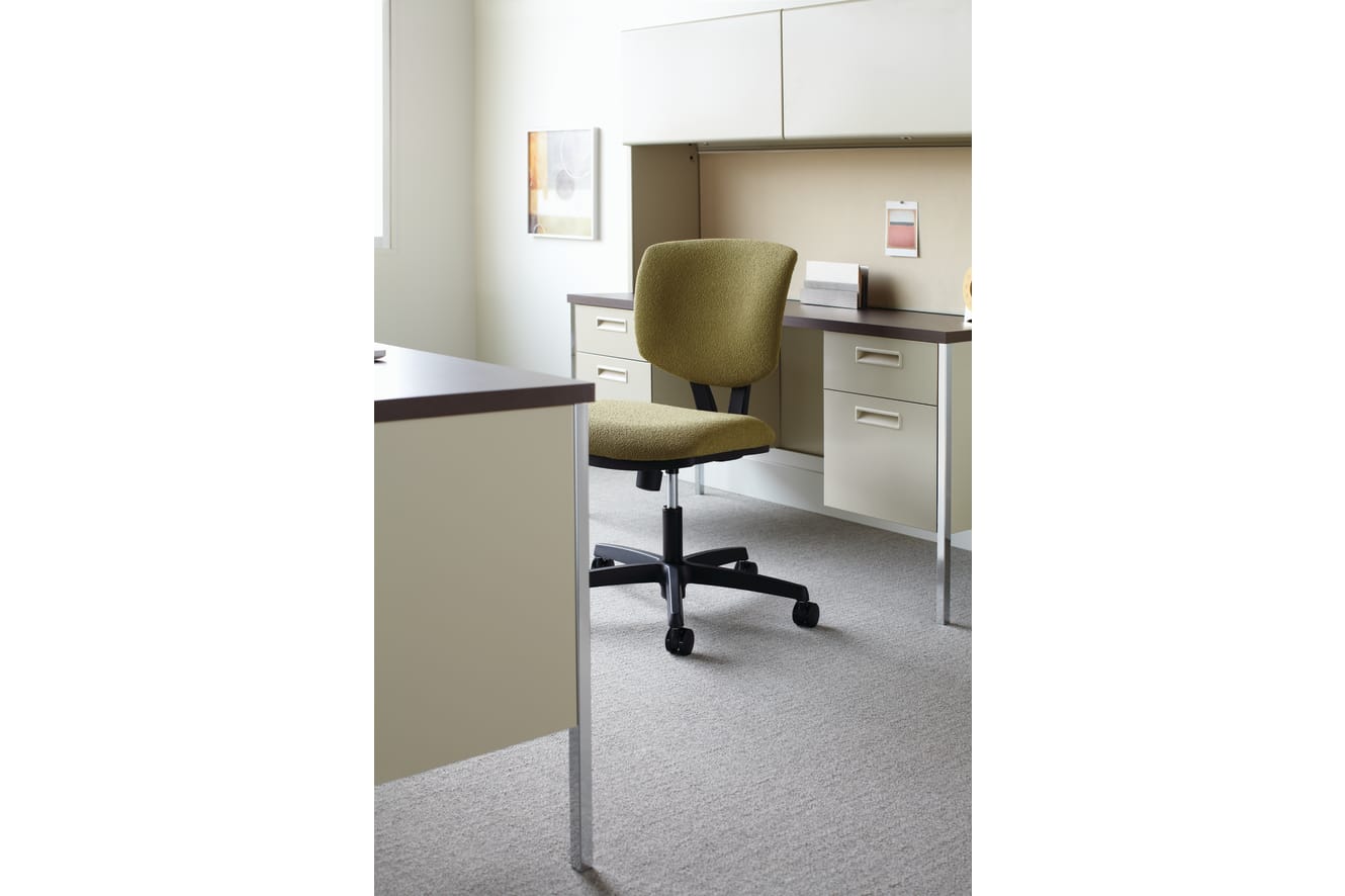 The image depicts an office workspace with a desk, a green upholstered office chair, and various storage units in the background.