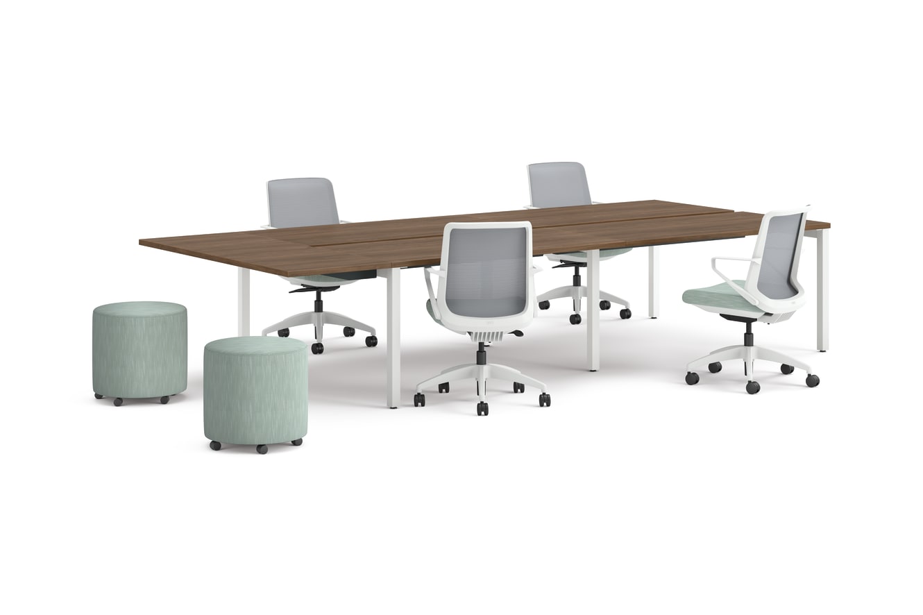 Four ergonomic office chairs around two connected rectangular desks with wooden tops and white legs, accompanied by two round upholstered stools.