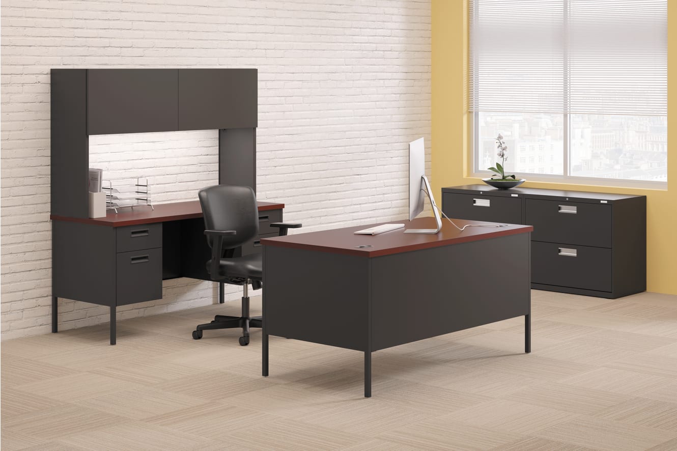 A modern and minimalist office setup with a black desk, a computer monitor, and a filing cabinet against a white brick wall background.