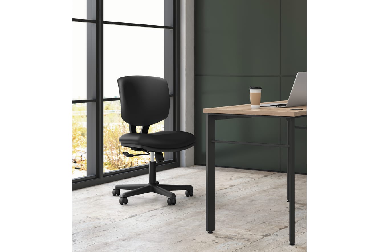 A modern, minimalist office space with a black office chair and a wooden desk near a large window overlooking a natural landscape.