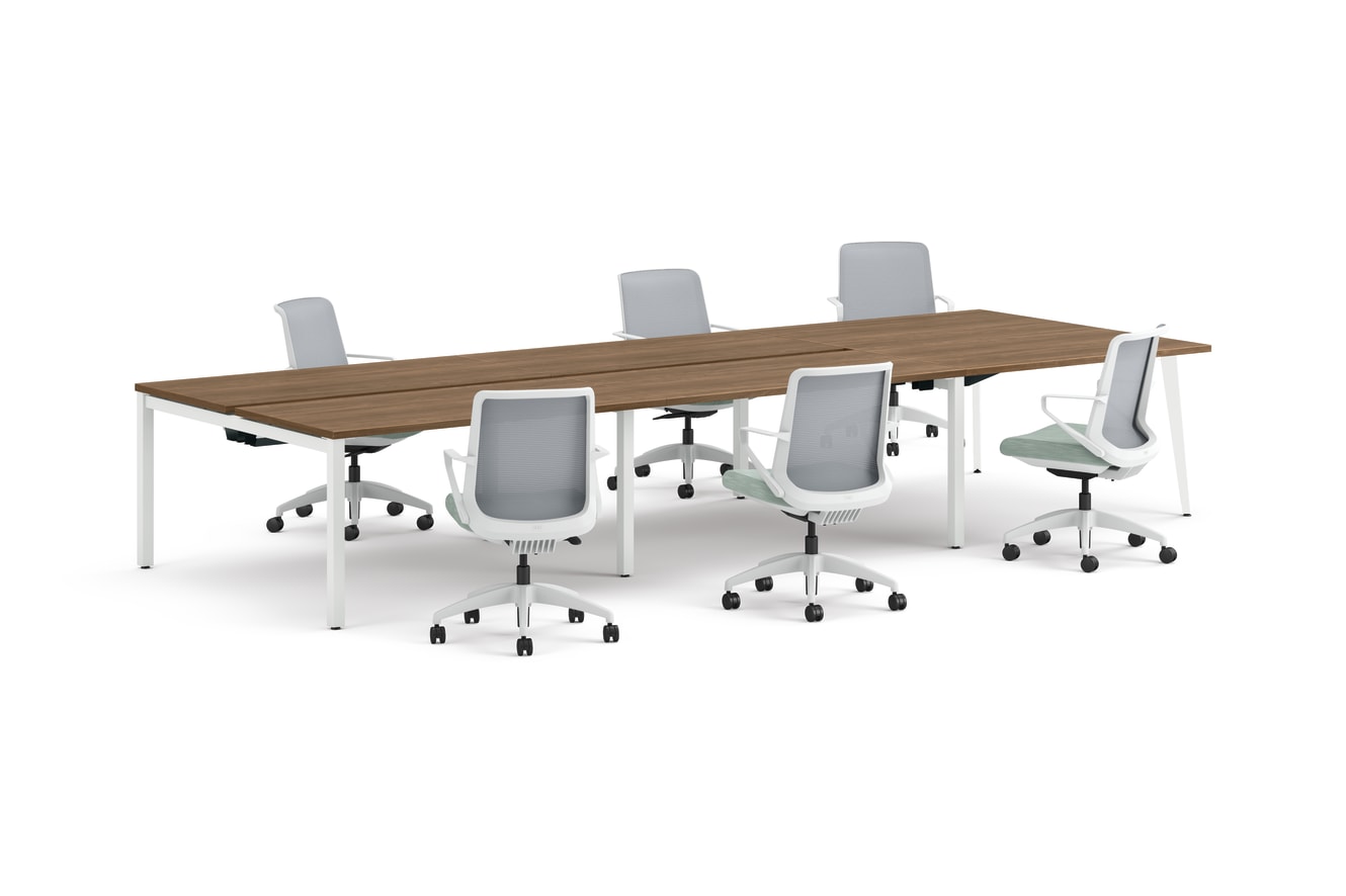 Six ergonomic office chairs arranged around two connected rectangular desks with wooden tops and white legs.