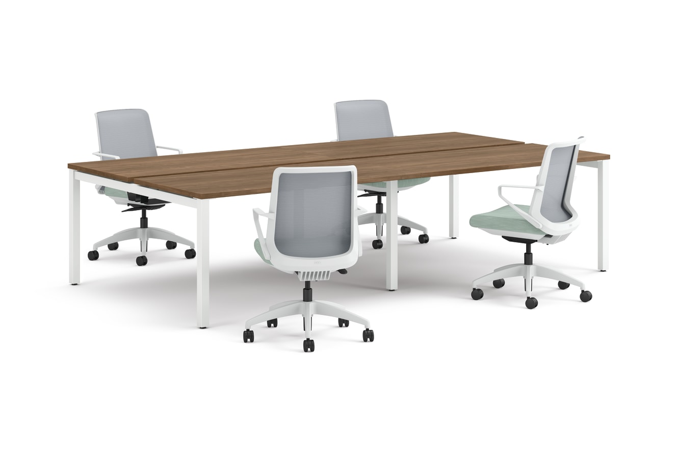 Four ergonomic office chairs arranged around two connected rectangular desks with wooden tops and white legs.