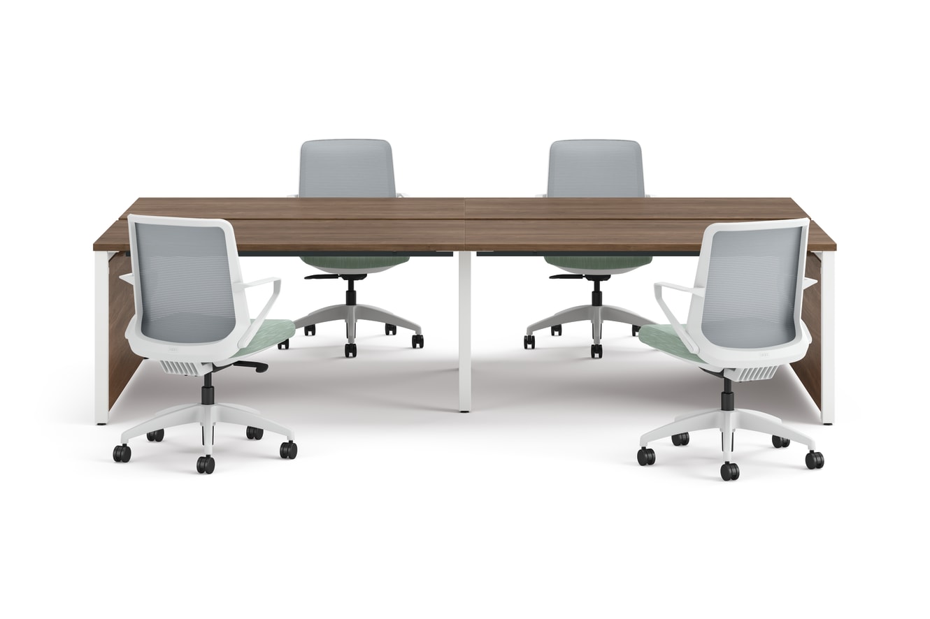 Four ergonomic office chairs arranged around two connected rectangular desks with wooden tops and white legs.