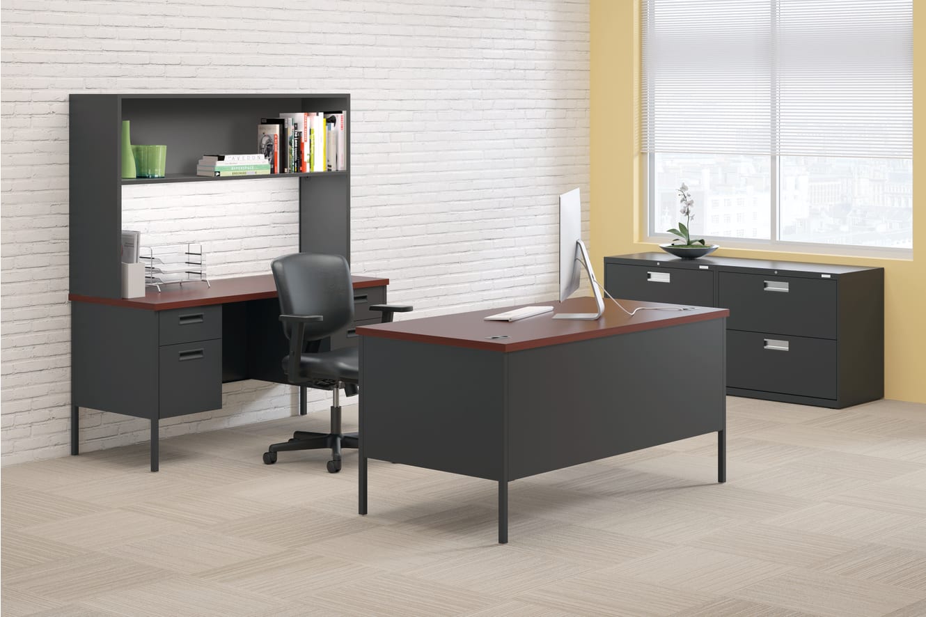 A modern and minimalist home office setup with a black desk, shelving unit, and filing cabinet against a white brick wall, providing a clean and organized workspace.