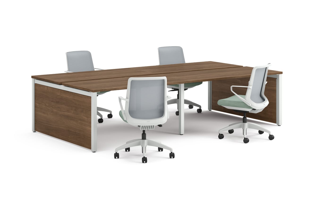 Four ergonomic office chairs arranged around two connected rectangular desks with wooden tops and white legs.