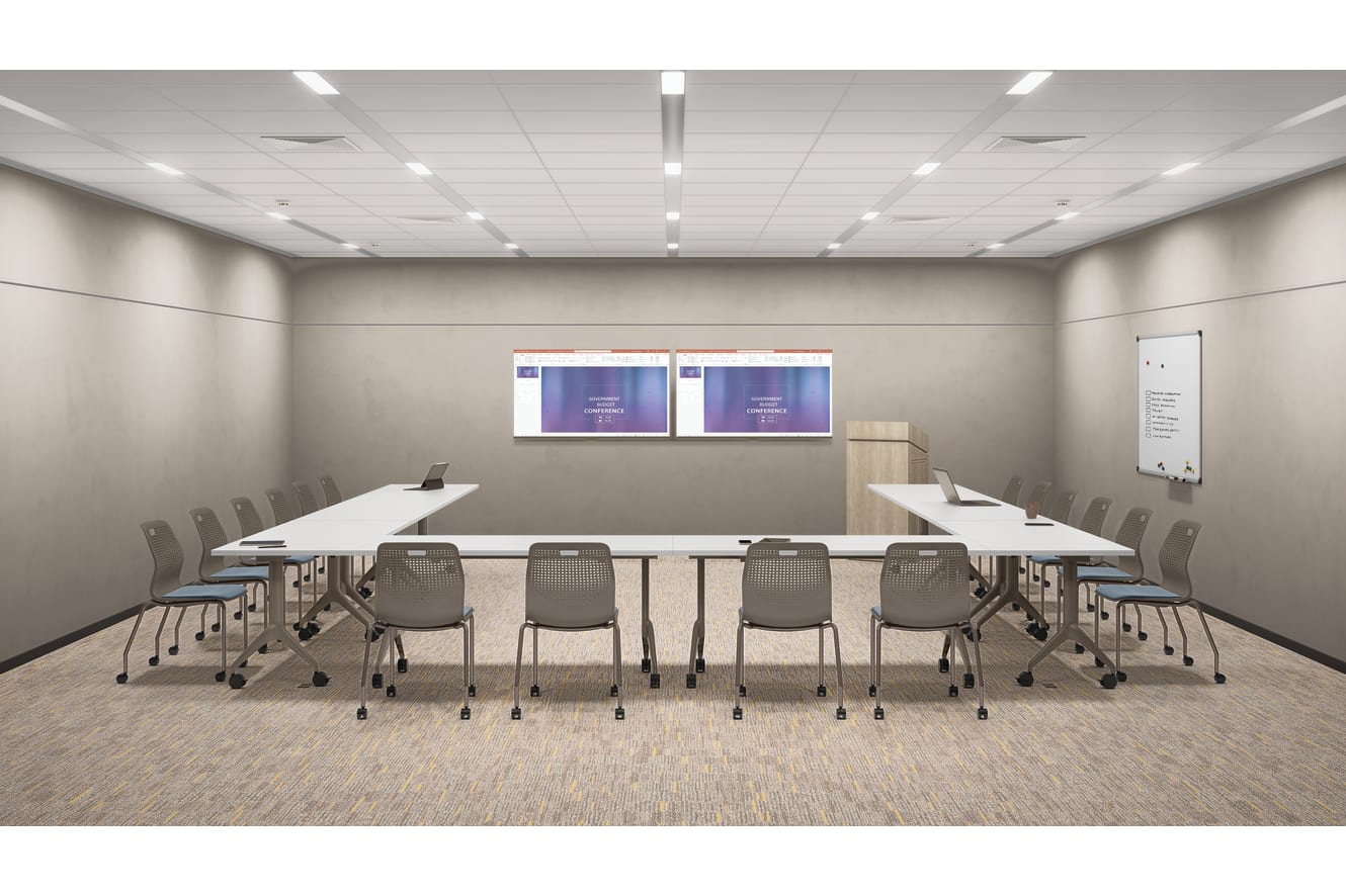 Modern training room with U-shaped tables, stackable chairs on casters, dual wall-mounted displays, lectern, whiteboard, and recessed ceiling lighting in a clean professional space.