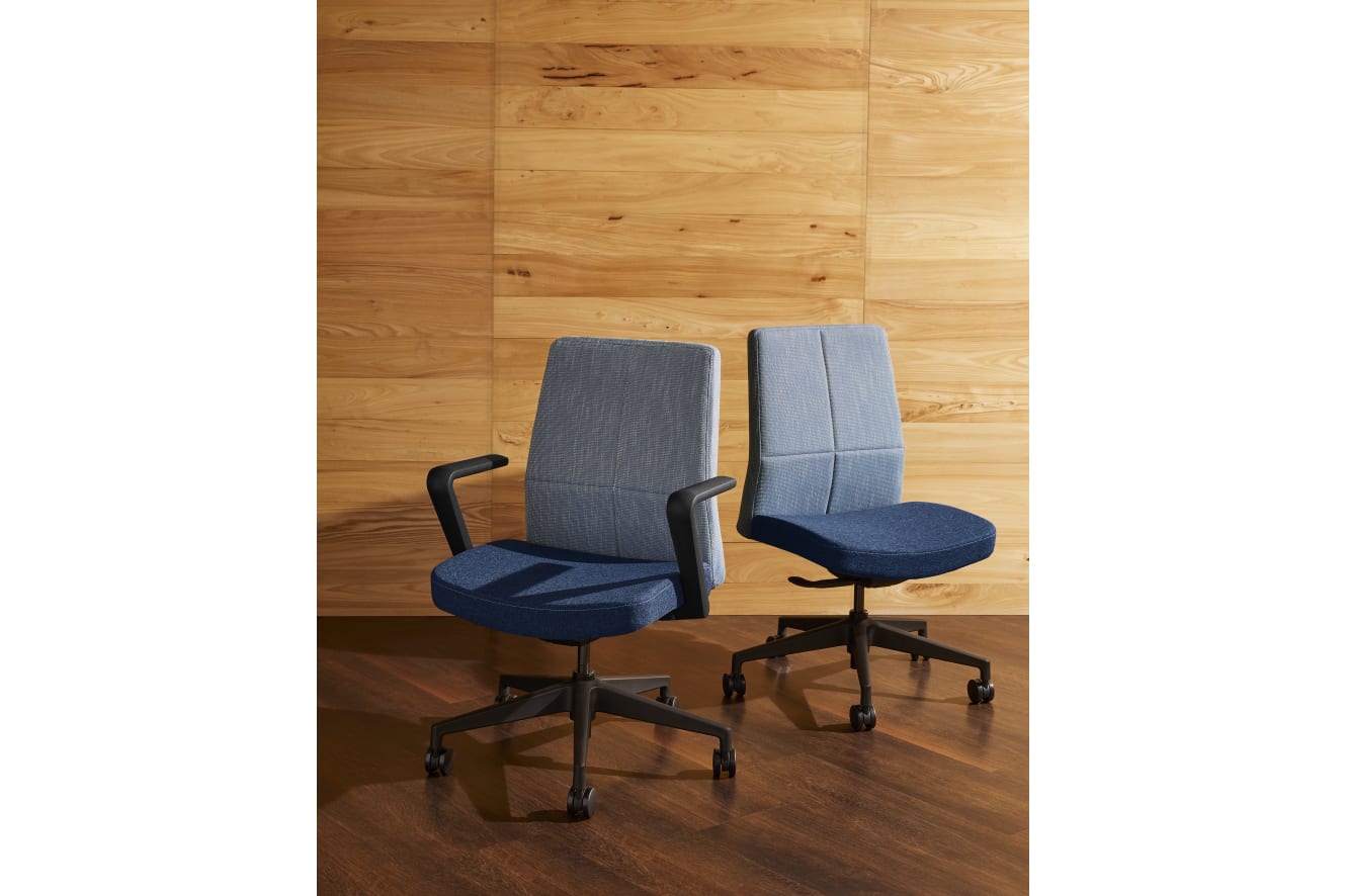 Two gray office chairs with armrests sit on a wooden floor against a wooden wall background.