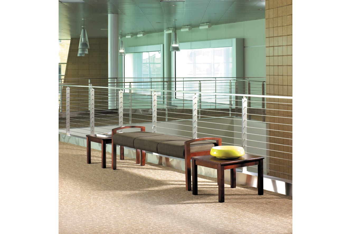 The image shows a modern, minimalist interior space with wooden benches and colorful cushions in the foreground, and a glass wall with metal railings in the background.