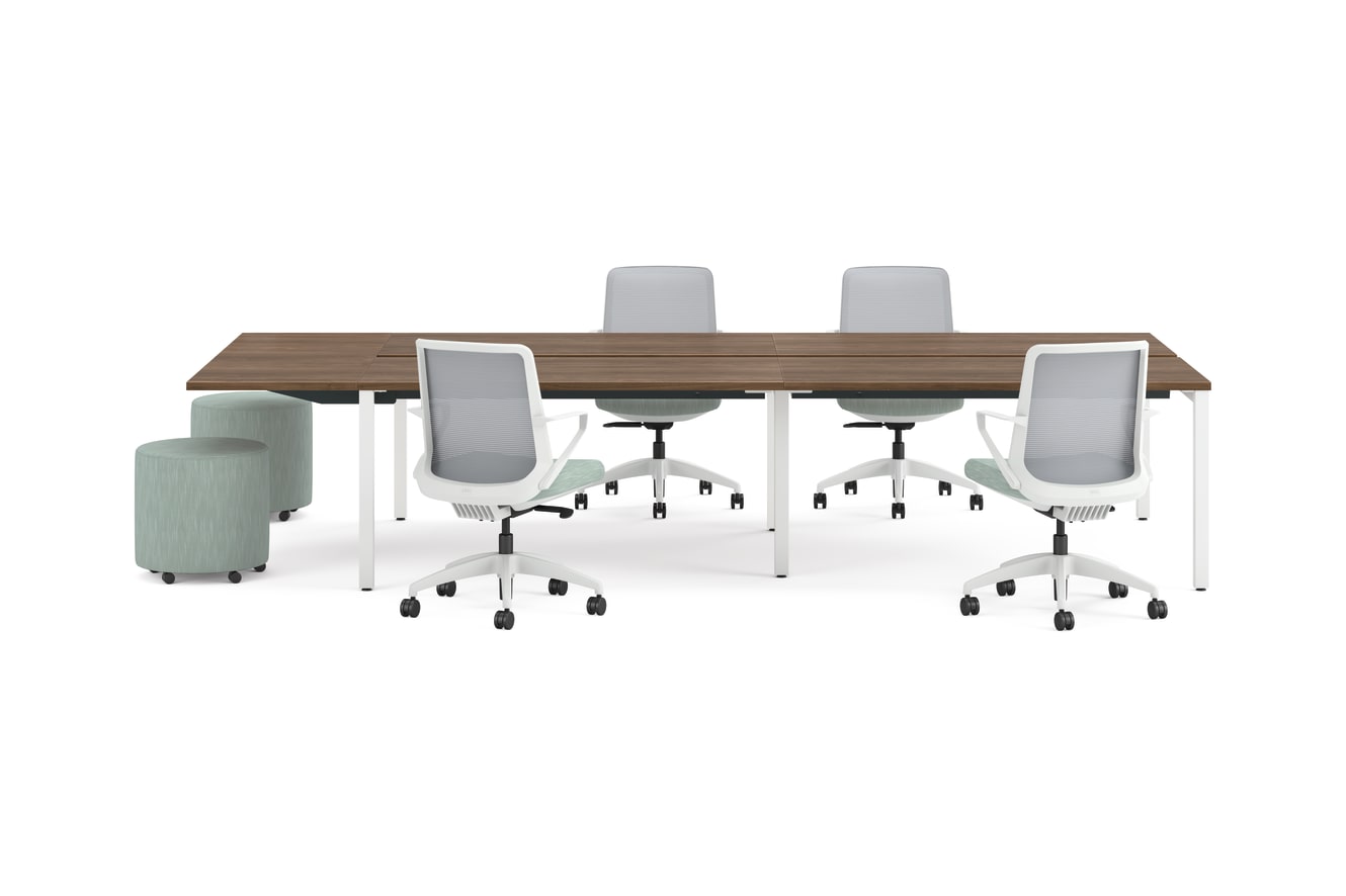 Four ergonomic office chairs around two connected rectangular desks with wooden tops and white legs, accompanied by two round upholstered stools.