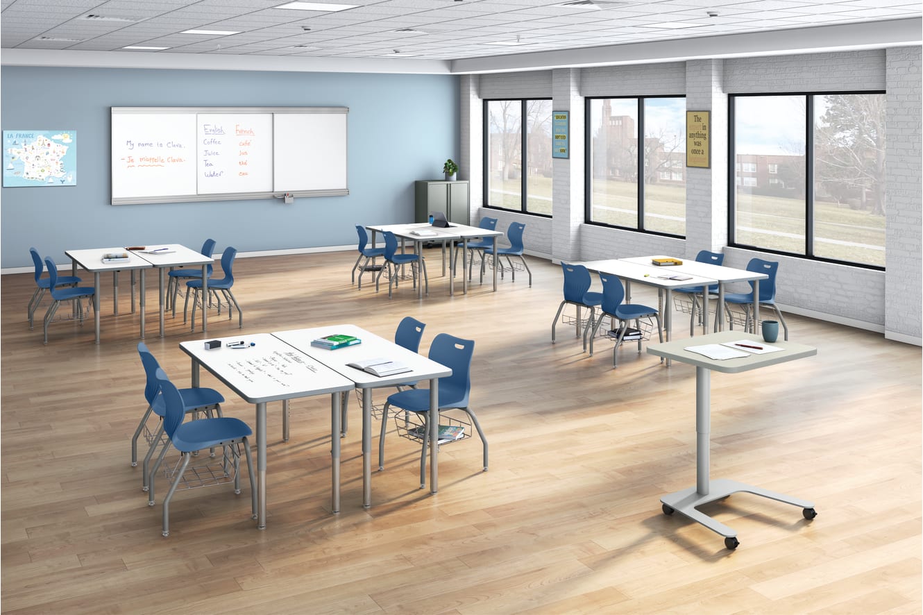 Modern classroom with grouped tables, blue chairs, large windows, educational posters, map of France, and whiteboard displaying English and French vocabulary.