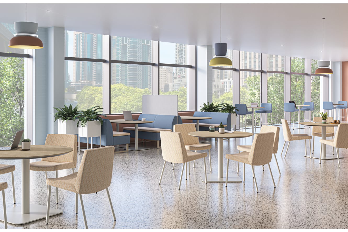 A bright, modern workplace cafeteria with floor-to-ceiling windows, round wooden tables, upholstered chairs, blue booth seating, and colorful pendant lights overlooking a city skyline.