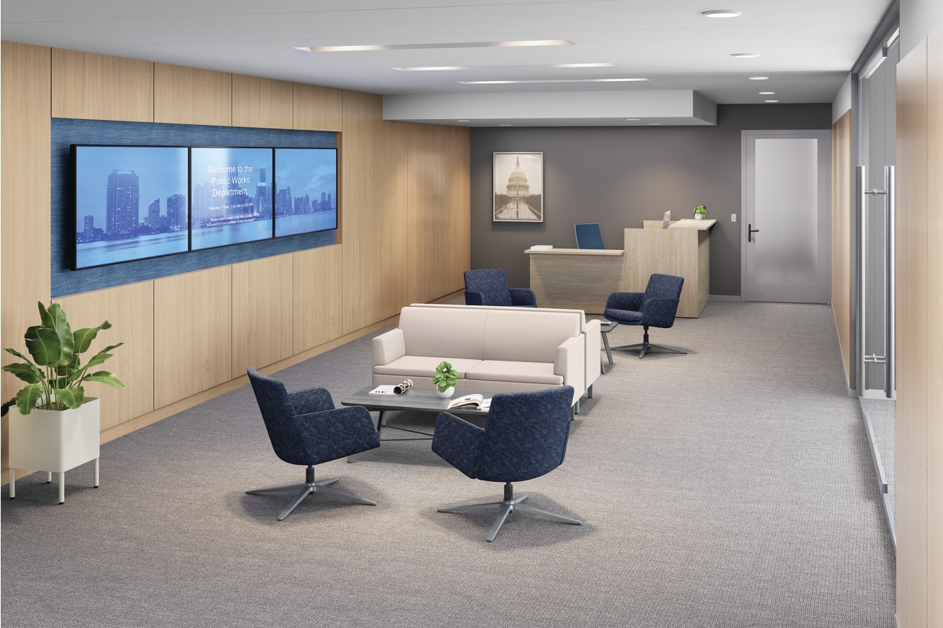 Modern office lounge with white sofa, blue lounge chairs, wall-mounted digital display, wood paneling, and reception desk.
