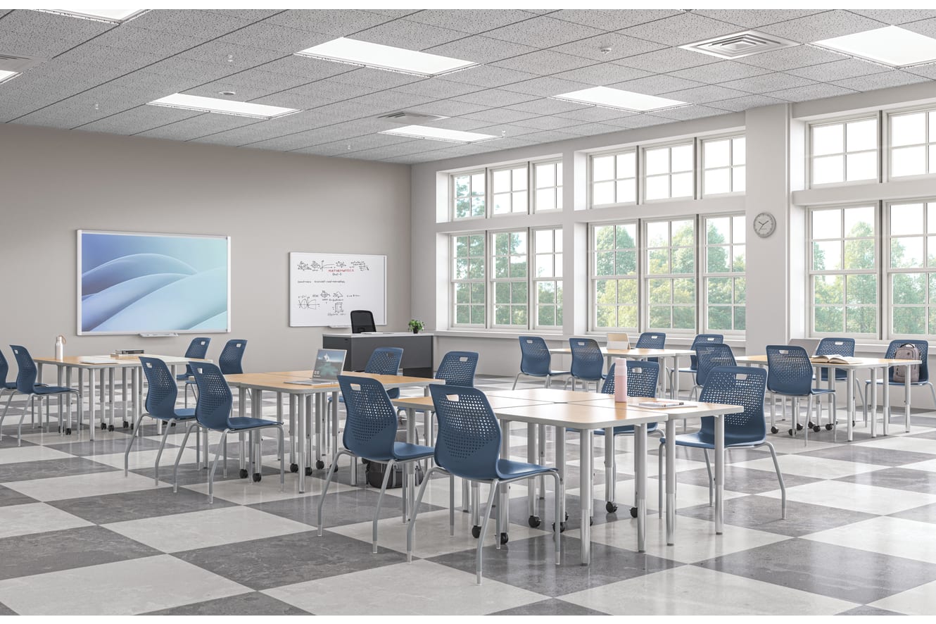 Bright modern classroom with movable tables, blue chairs, whiteboard displays, and large windows bringing in natural light.