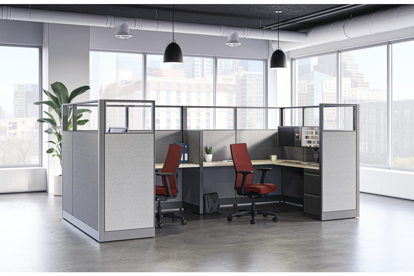Modern open office with four gray-paneled workstations, red task chairs, and large windows showing a city skyline.
