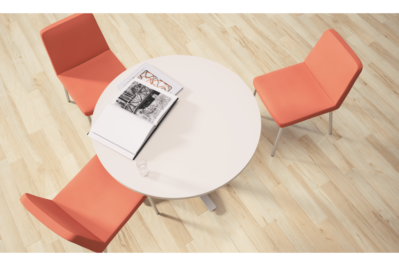 A round white table with a magazine on it, surrounded by four orange chairs on a wooden floor.