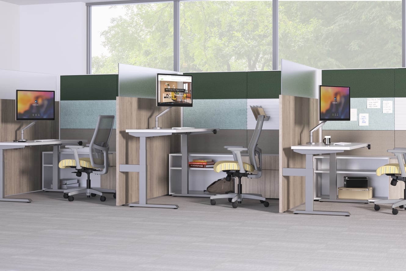 A modern, open-plan office space with multiple workstations, each equipped with a computer monitor, desk, and ergonomic chairs. The large windows in the background provide natural lighting and a view of the surrounding greenery.