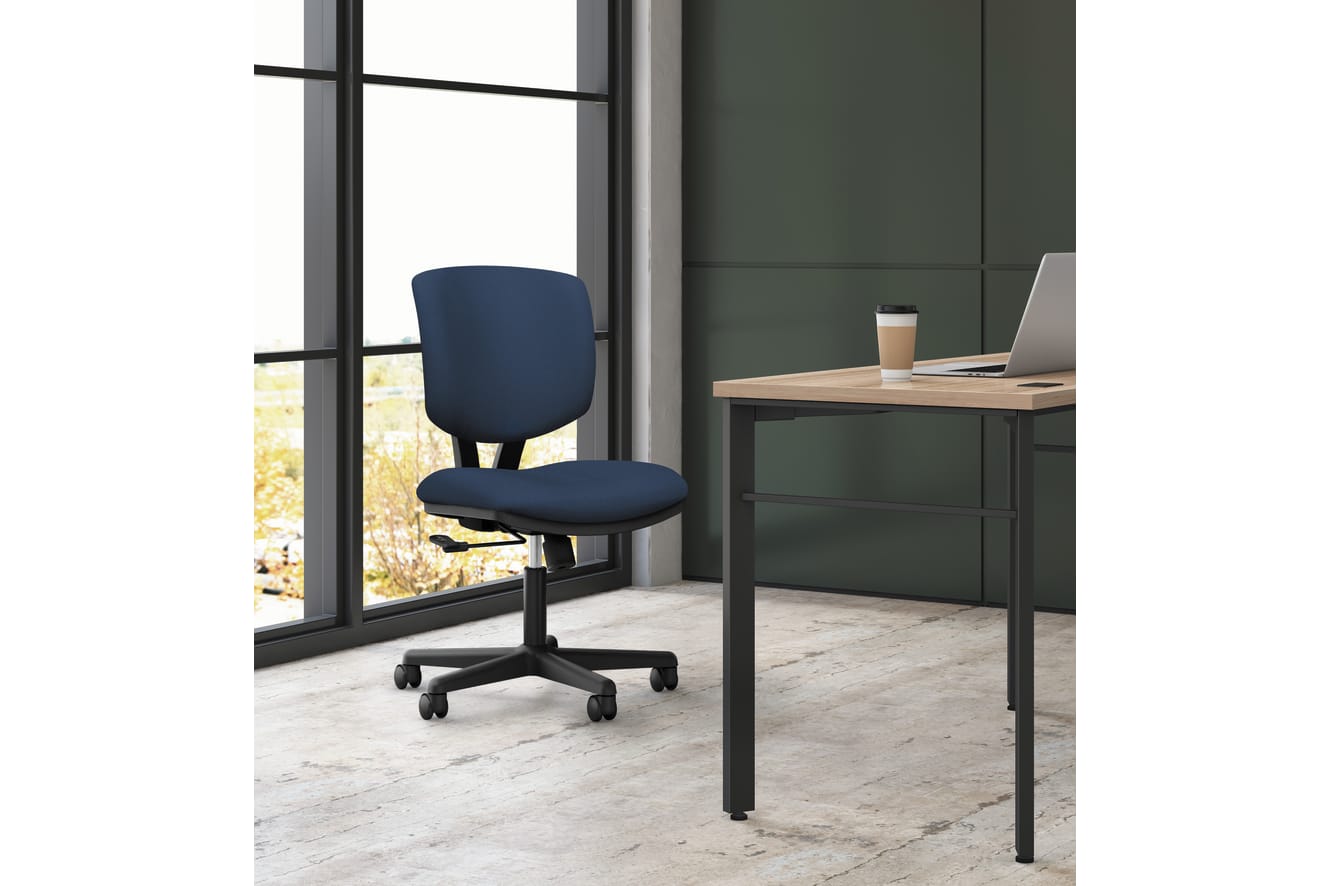 A modern office space with a navy blue office chair and a wooden desk with a laptop and a coffee cup placed on it, set against a large window overlooking a natural landscape.