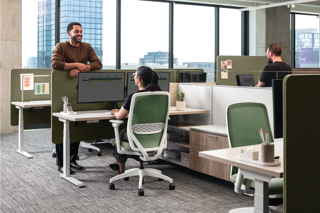 Open workstation cluster with height-adjustable desks, upholstered privacy panels, dual monitor setups, ergonomic task chairs, and integrated storage, complemented by bench seating with cushion top, personal lighting, and accessory trays.