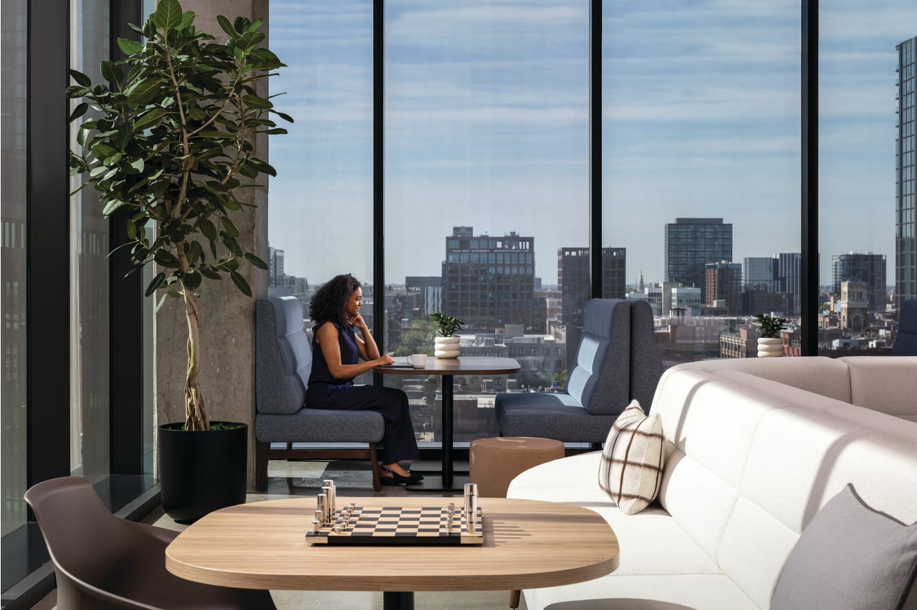 Modern lounge seating with small table, indoor plant, and floor-to-ceiling windows overlooking urban skyline.