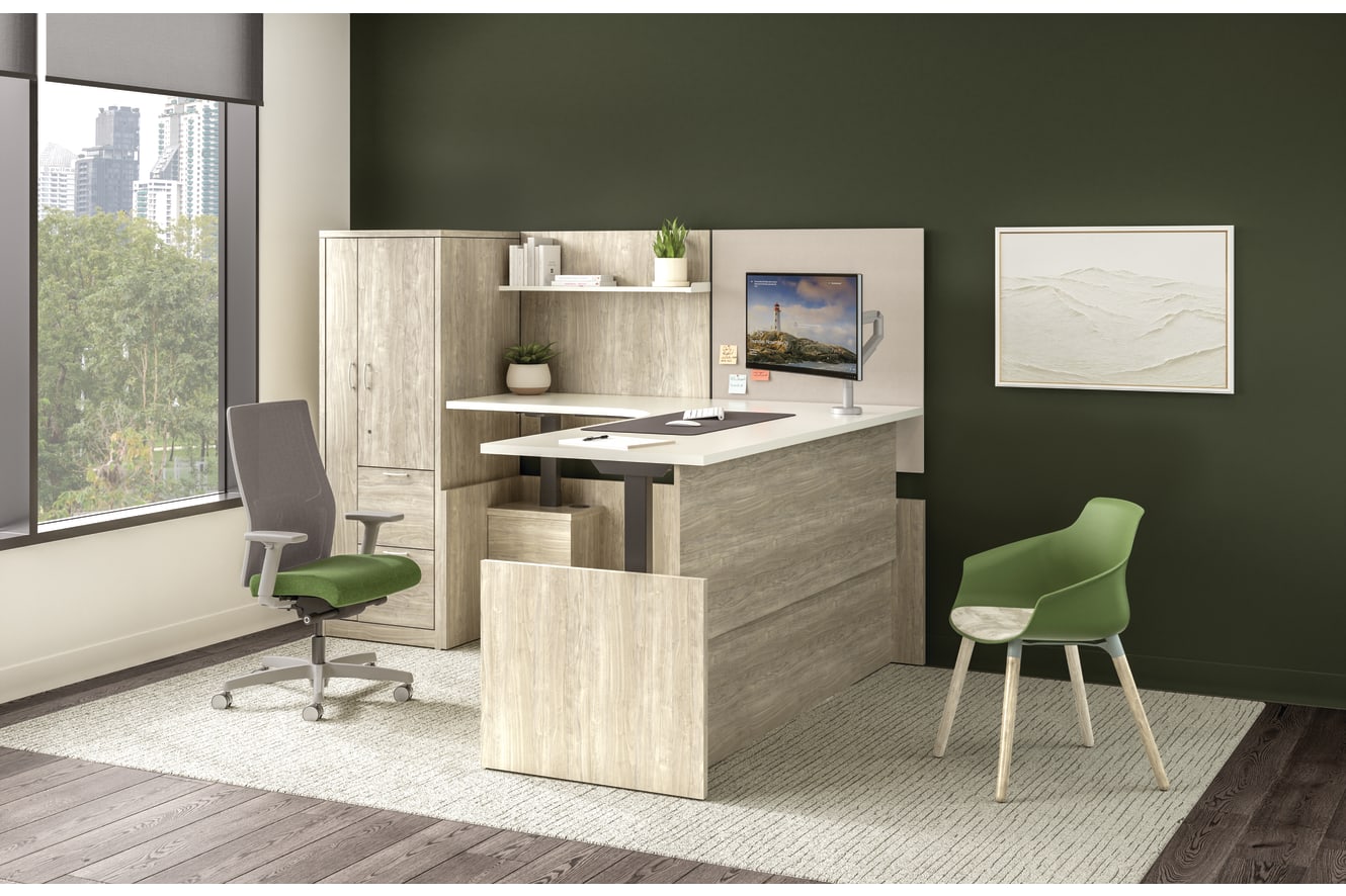 Private office with light wood desk, storage cabinet, return surface, task chair, guest chair, mounted monitor, and accent wall with window view.