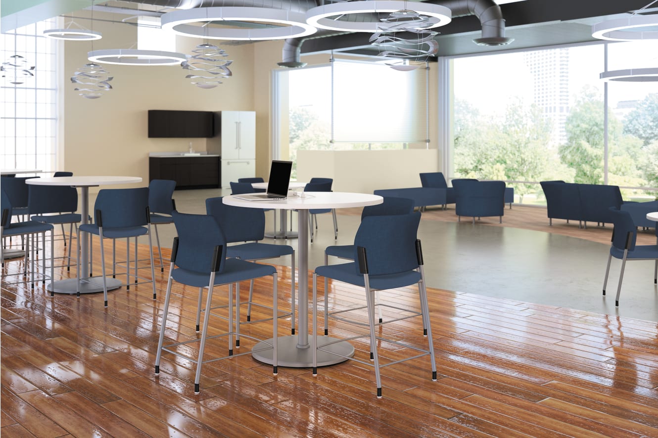 A modern and spacious office or meeting space with high ceilings, large windows, and sleek furniture including round tables and black chairs arranged in a casual, collaborative setup.