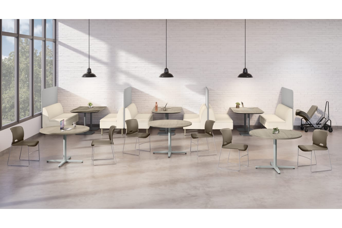 An open dining area with round tables, chairs, booth seating, hanging pendant lights, and large windows allowing natural light into the space.