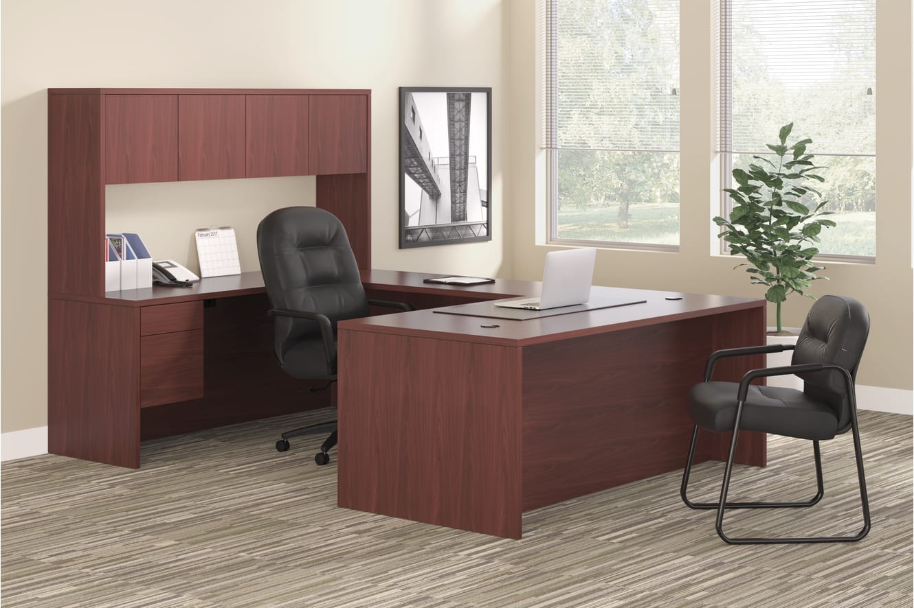 A modern and minimalist office setup with a wooden desk, a computer, and a bookshelf in the background, situated in a well-lit room with a large window overlooking a natural landscape.