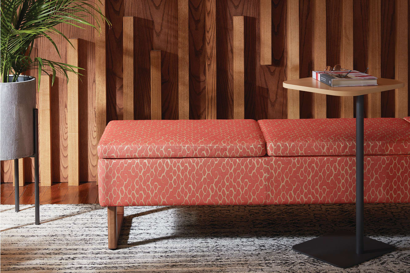 A cozy red patterned sofa sits on a wooden floor against a backdrop of vertical wooden panels, with a potted plant and a side table nearby.