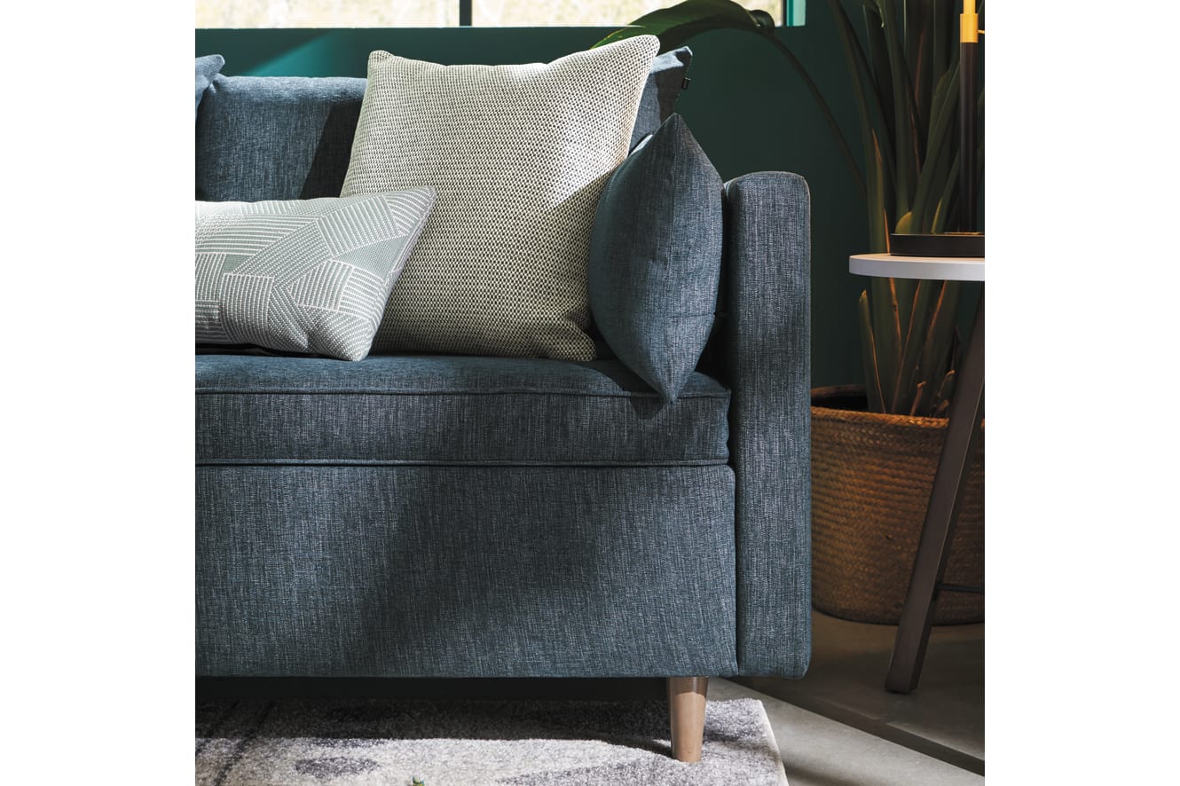 A cozy gray sofa with plush pillows sits in a warm, inviting living space, surrounded by natural elements like potted plants and a woven basket.