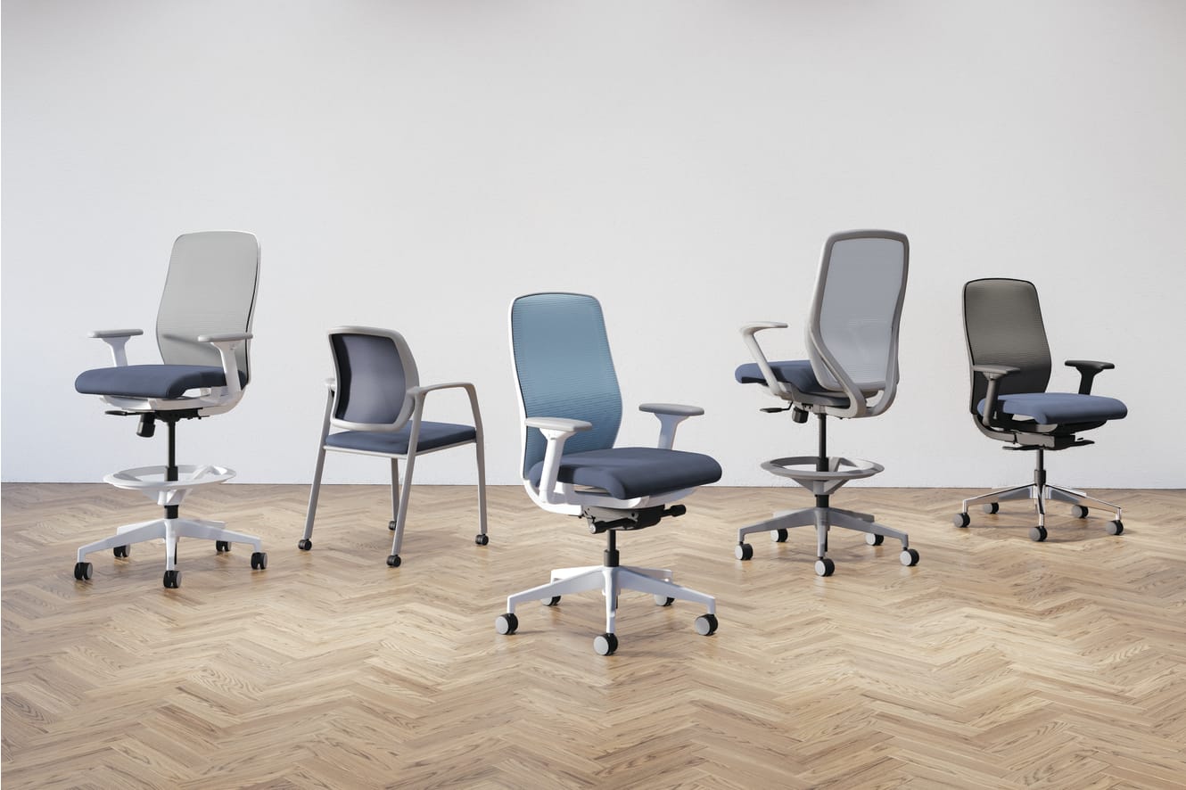 A collection of modern, adjustable office chairs in various shades of gray and blue, arranged on a herringbone-patterned wooden floor against a plain background.