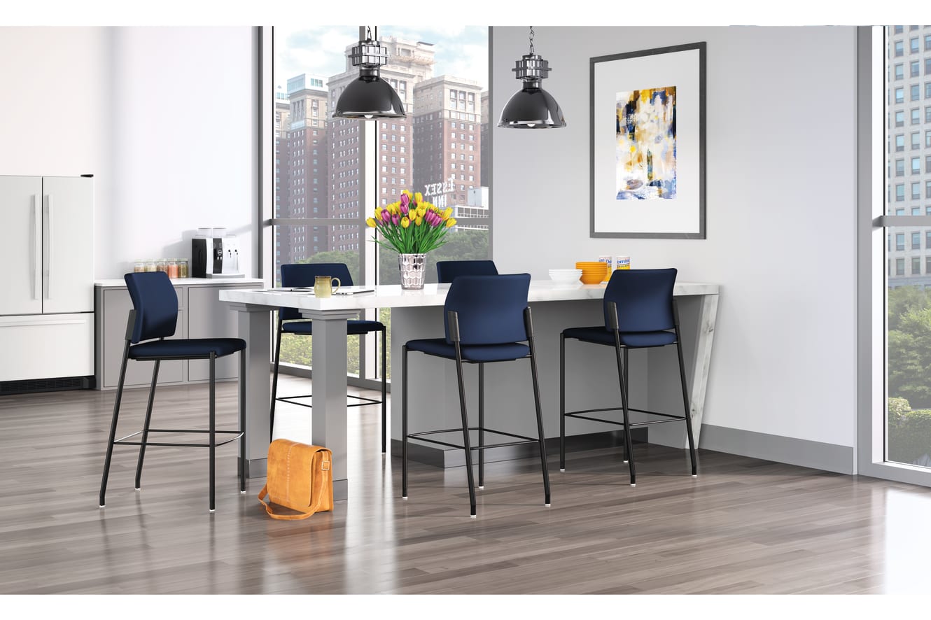 A modern and stylish dining area with a sleek white table, navy blue bar stools, and large windows overlooking a cityscape in the background. The room is accented with industrial-style pendant lights and a vibrant floral arrangement on the table.