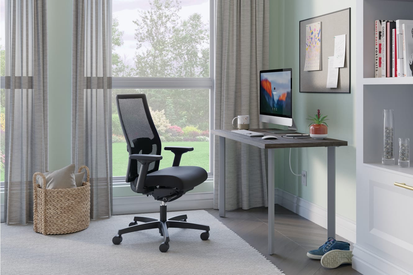 A modern and minimalist home office setup with a comfortable office chair, a desk with a computer monitor, and various decor elements such as artwork and plants, all set against a large window overlooking a natural outdoor scene.