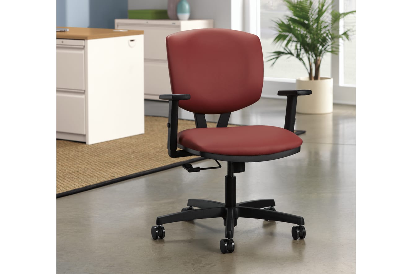 A red office chair with adjustable armrests sits on a tiled floor, with a filing cabinet and a potted plant visible in the background.