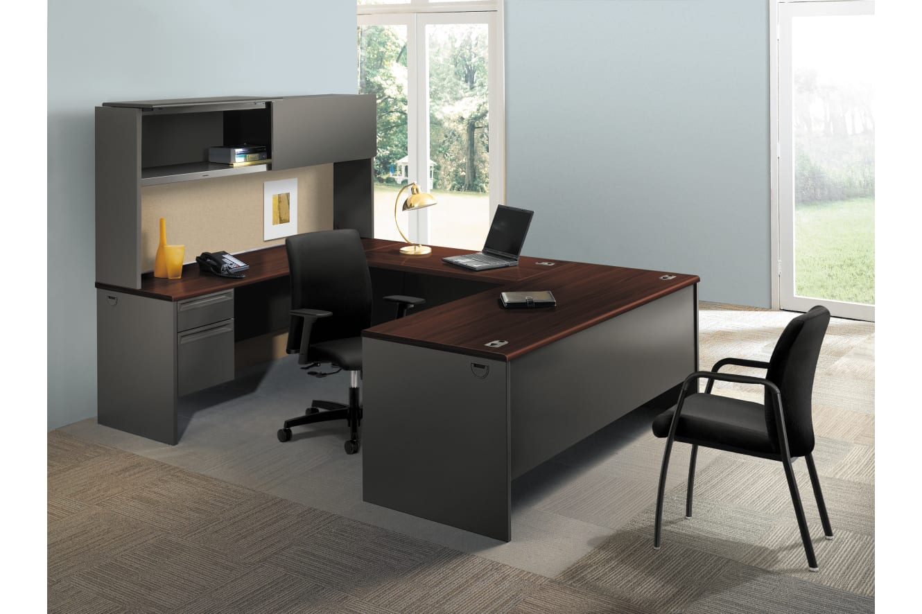 A modern and minimalist home office setup with a large wooden desk, a black office chair, and a storage unit with shelves and drawers, all set against a bright and airy background with a large window overlooking the outdoors.