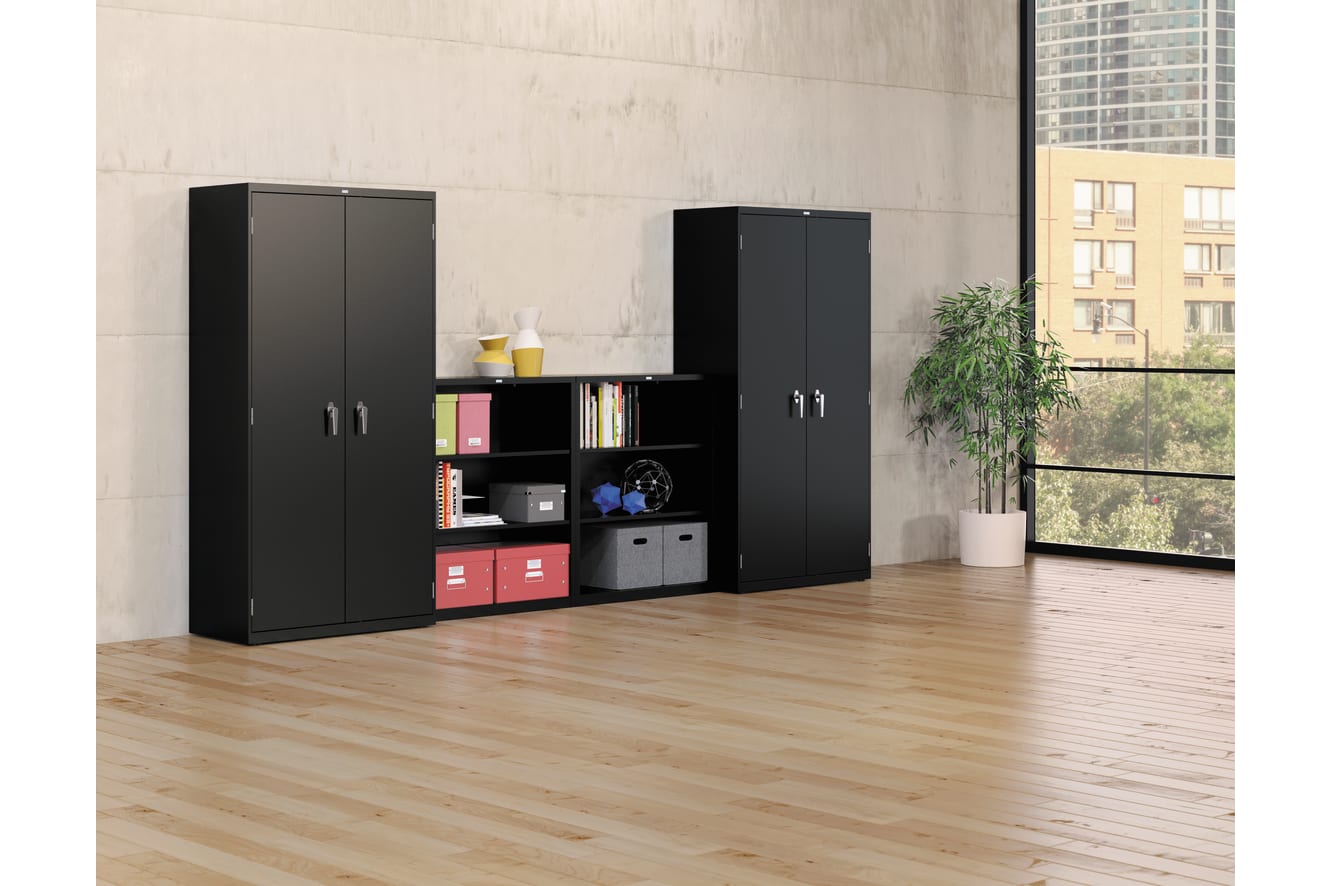 The image depicts a modern and minimalist home office or study space, featuring black storage cabinets and shelves against a plain white wall, with a large window providing natural light and a view of the outdoors.