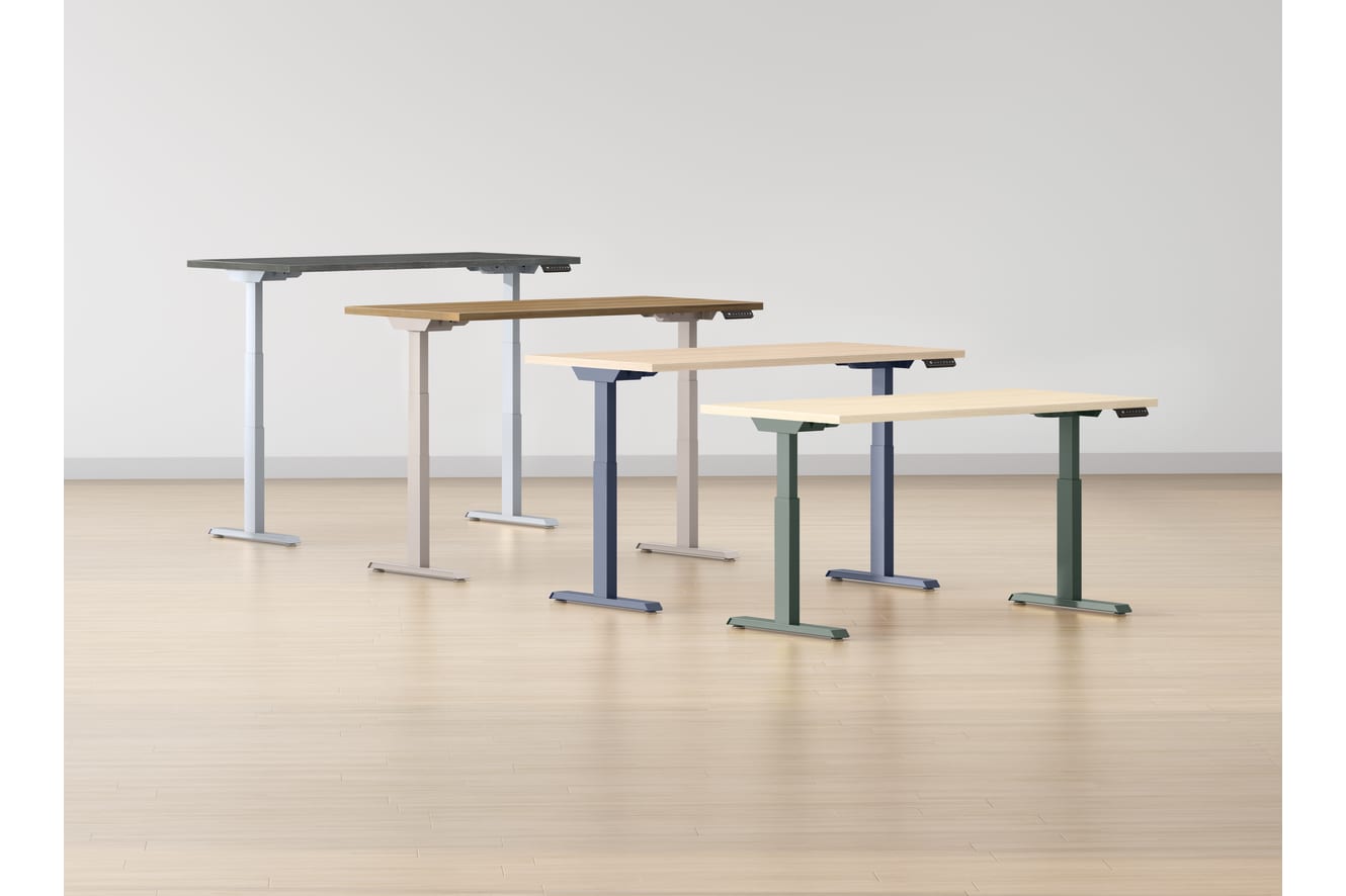 A collection of adjustable standing desks or workstations in various sizes and colors, arranged on a wooden floor against a plain white background.