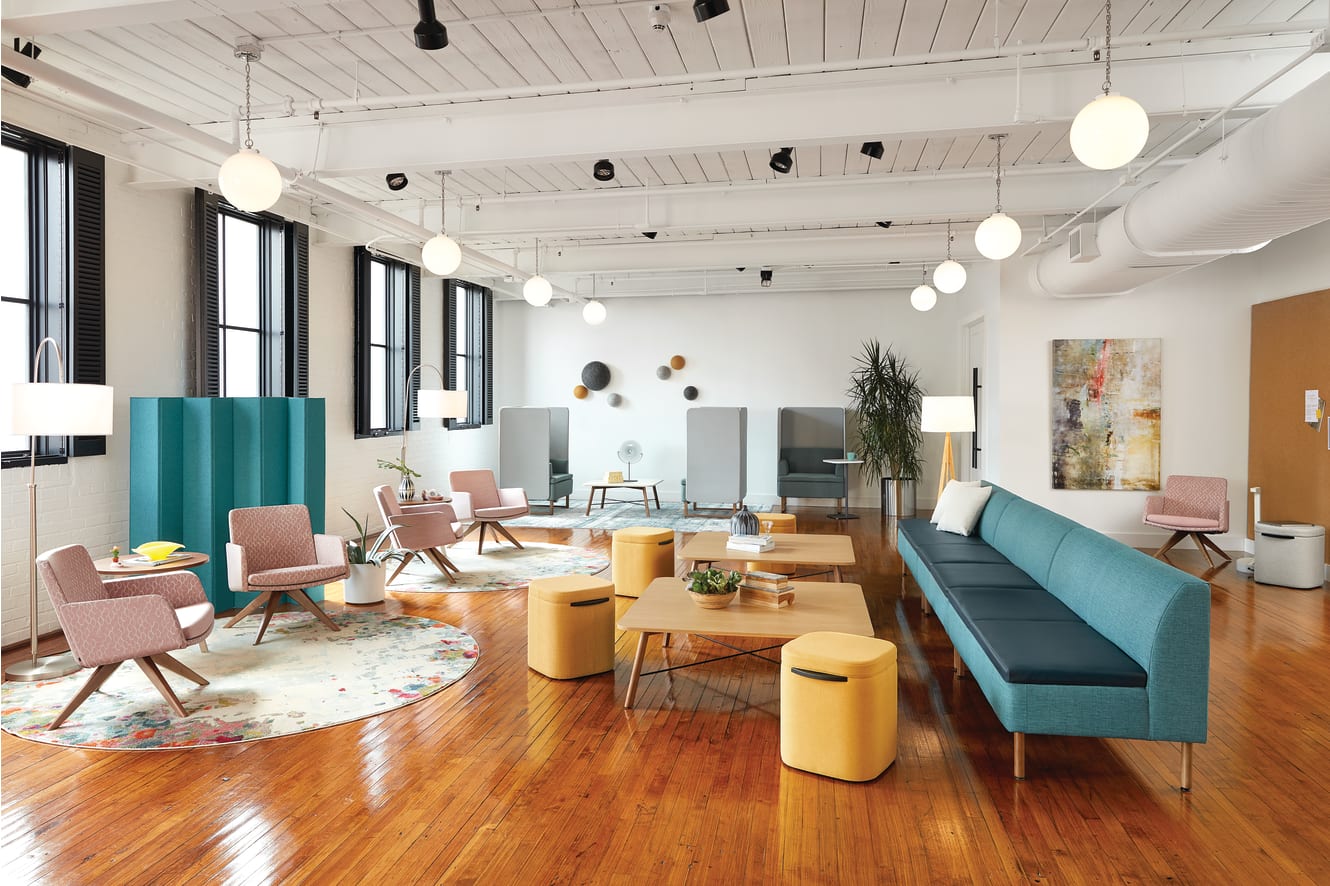 A modern and vibrant office space with a mix of comfortable seating, colorful accents, and natural lighting from the large windows.
