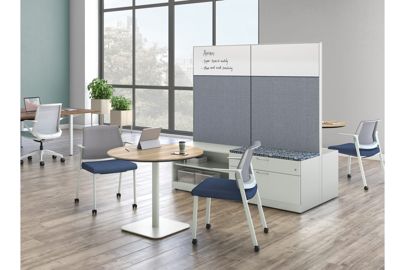 A modern and minimalist office space with a whiteboard, desks, chairs, and potted plants, set against a backdrop of large windows overlooking an outdoor scene.