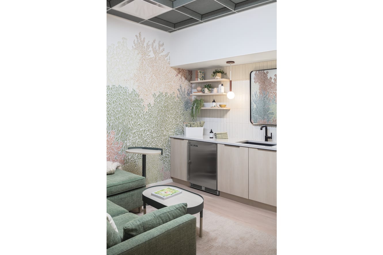 Lounge area with upholstered armchairs, soft seating, nested tables, side table, built-in cabinetry with integrated refrigeration, open shelving, pendant lighting, and decorative wall panels.