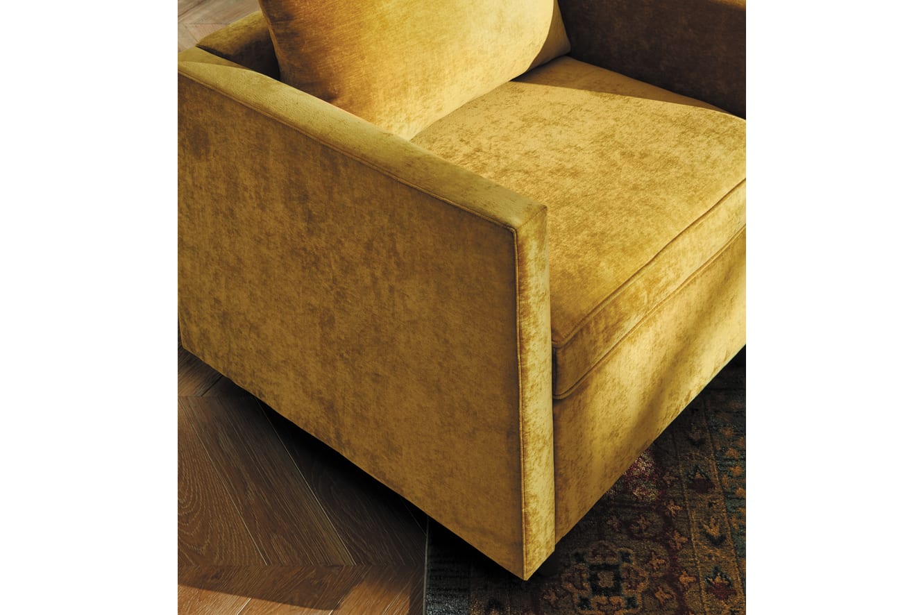 A plush, mustard-colored sofa sits on a patterned rug, with the wooden floor visible in the background.
