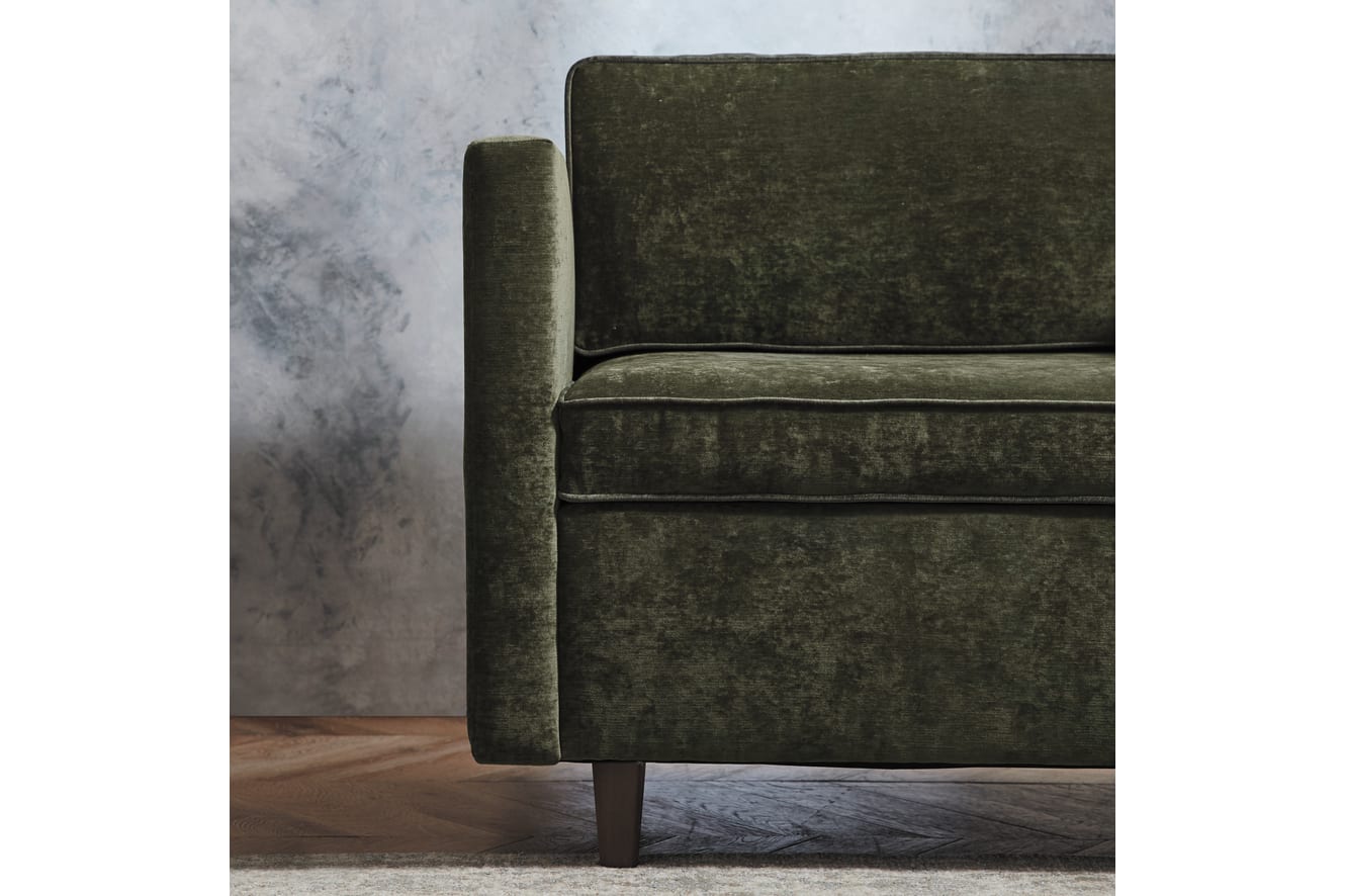 A dark green velvet sofa sits on a wooden floor against a gray background, creating a cozy and inviting atmosphere.
