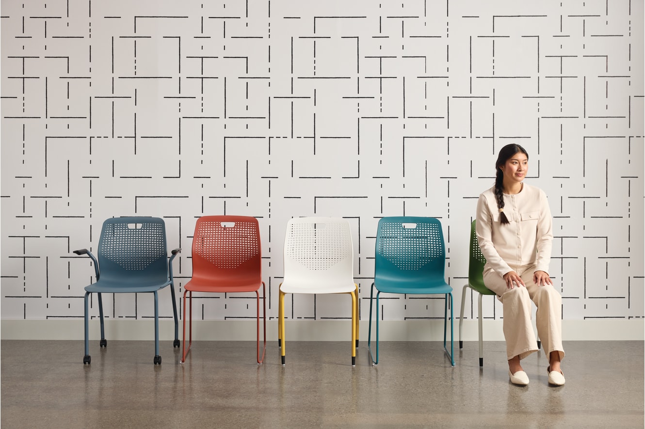 The image features a woman standing in front of a patterned wall, with four colorful chairs arranged in the foreground.