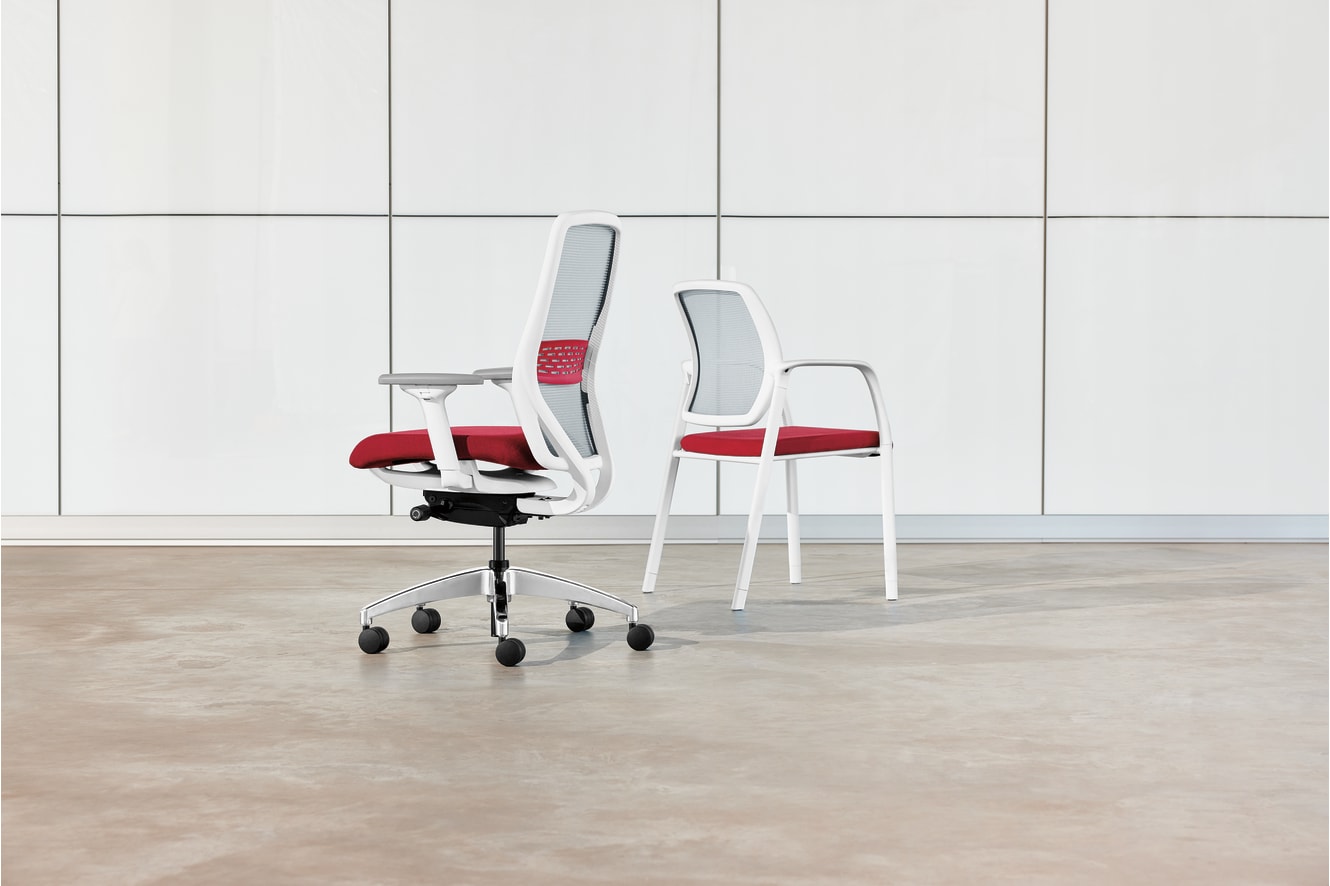 The image shows a modern office chair and two matching chairs in a minimalist, white-tiled room.