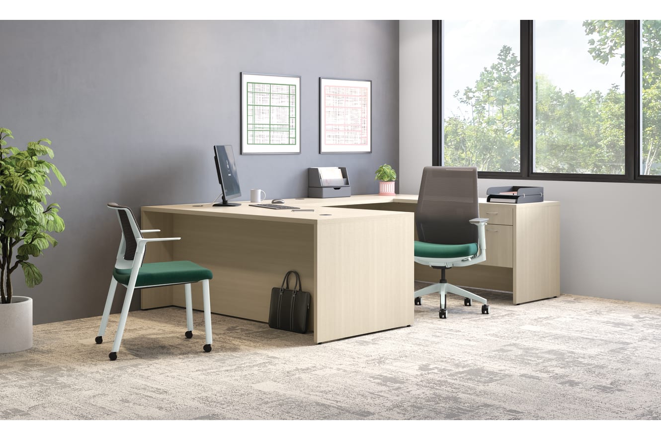 Contemporary office with L-shaped wooden desk, ergonomic chair, guest chair, computer monitor, and large window with outdoor view.