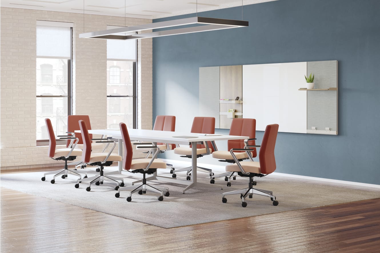 A modern and minimalist conference room with a long wooden table surrounded by red office chairs, a large mirror on the wall, and a sleek lighting fixture overhead.