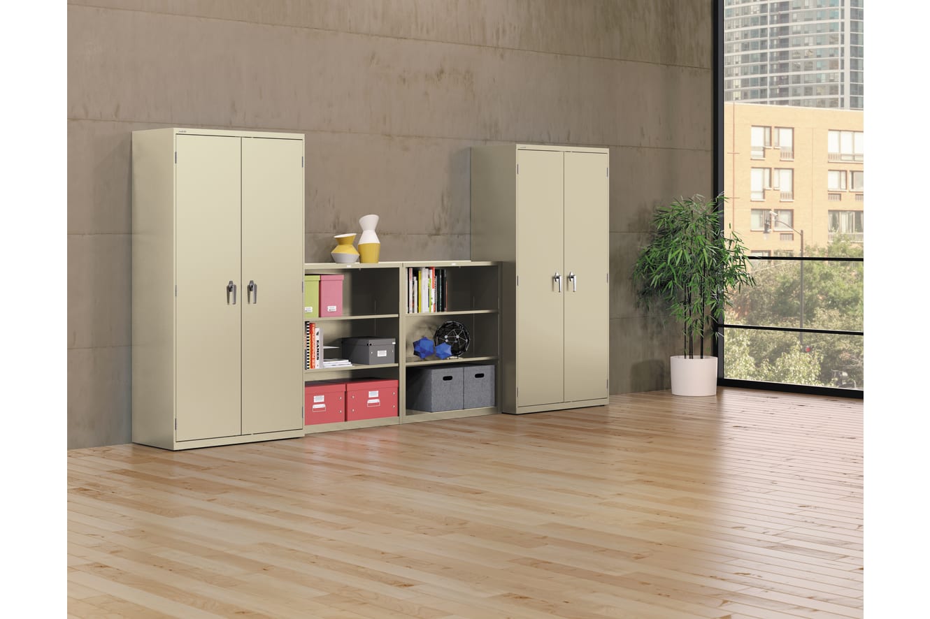 The image depicts a modern, minimalist office or home interior with beige cabinets, shelves, and a potted plant, set against a plain concrete wall and wooden flooring.