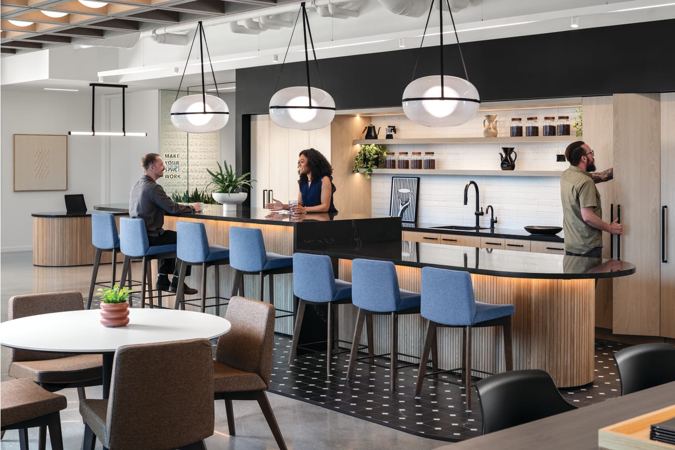 Round meeting table with upholstered guest chairs and adjacent counter-height chairs on wood legs, featuring cushioned seats and backs for collaborative seating.
